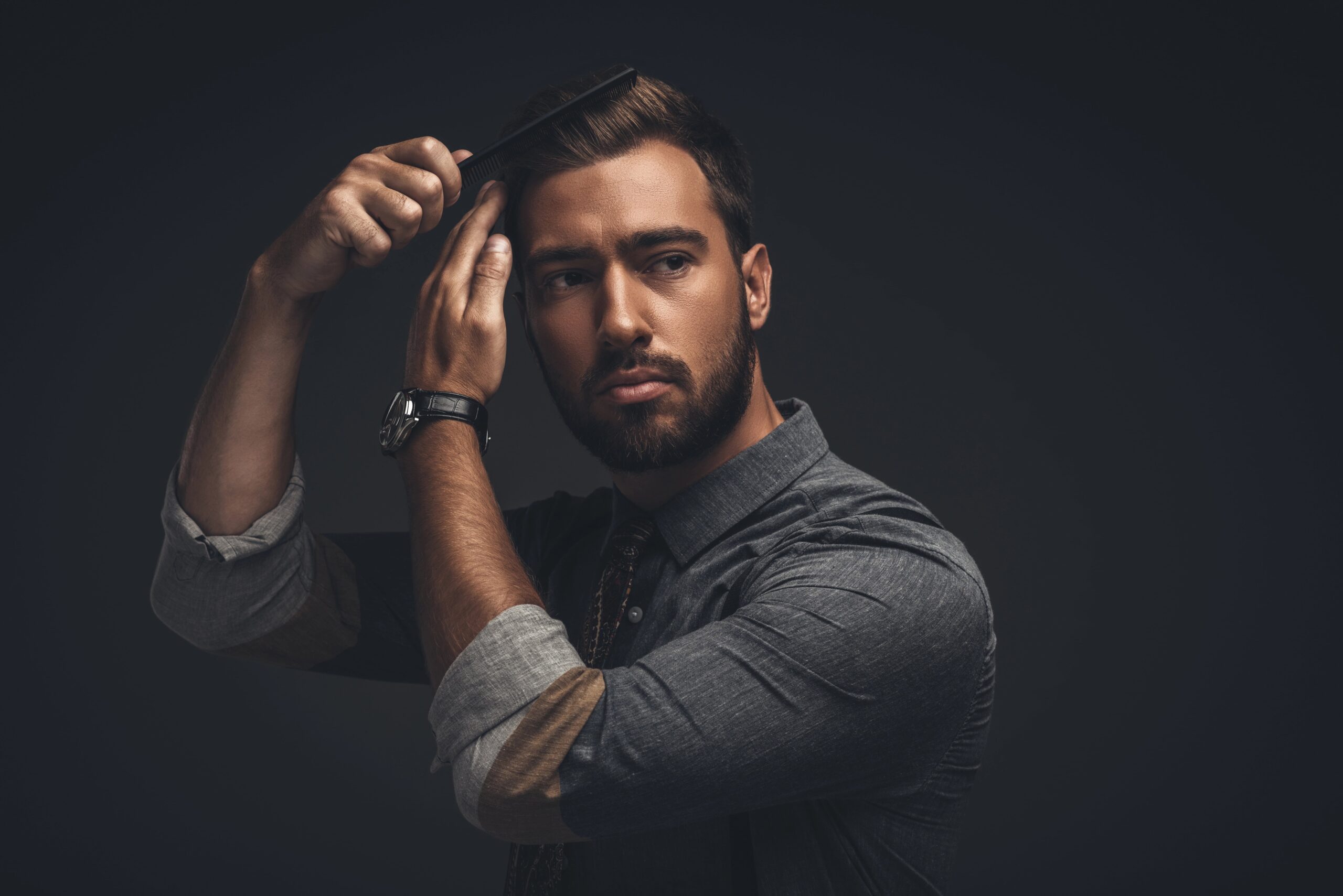 Handsome man styling his hair, black background