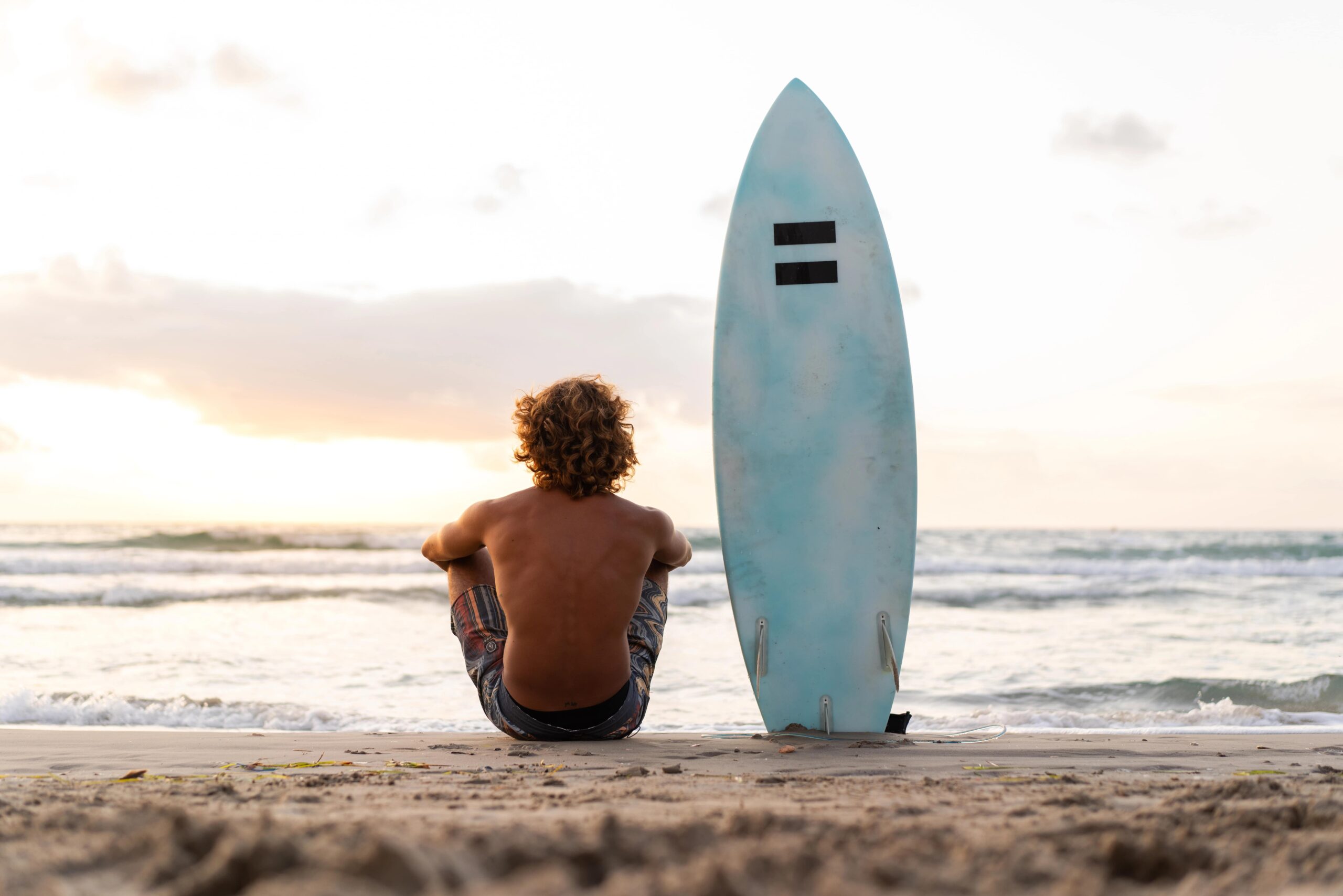 Young male surfer sitting beside board on beach