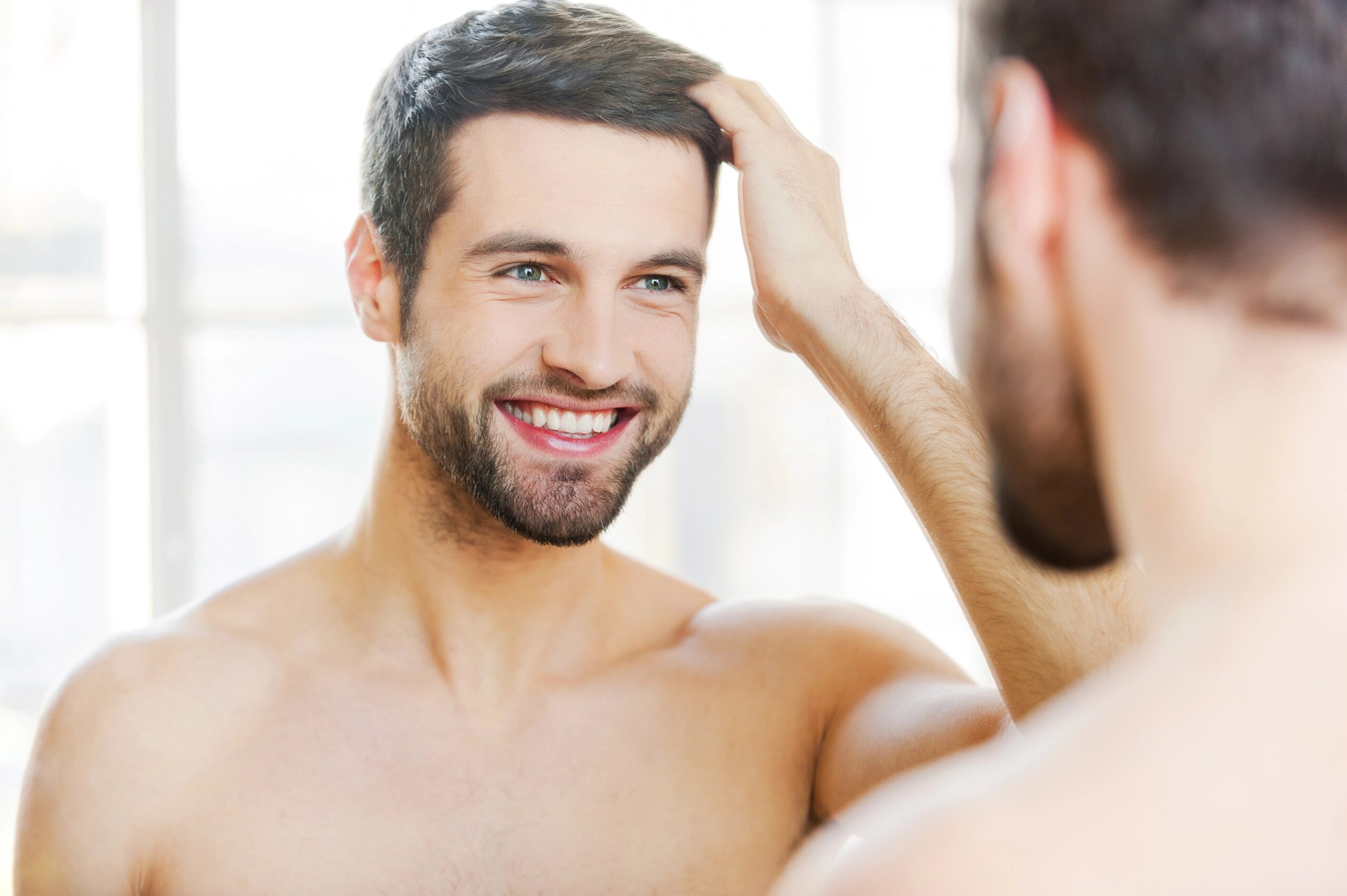 Smiling young man looking at hair in bathroom mirror